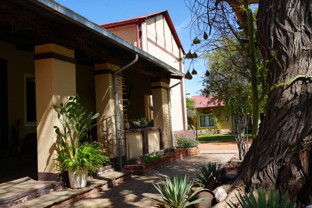 Namibisches Farmhaus mit angrenzendem Garten, grünem Rasen und Schatten spendenden Bäumen