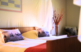 Helles Gästezimmer auf der Jagdfarm Krumneck in Namibia mit Doppelbett, dekorativen Kissen und stilvoller Vase