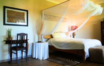 Komfortables Gästezimmer auf der Jagdfarm Krumneck in Namibia mit Doppelbett, Moskitonetz, Holzmöbeln und afrikanischen Dekorationselementen.