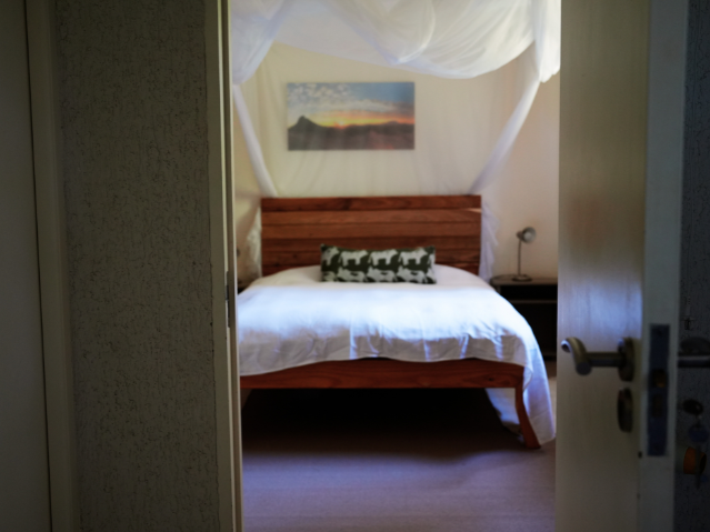 Schlafzimmer mit Holz-Himmelbett, weißer Bettwäsche und afrikanischem Dekor.