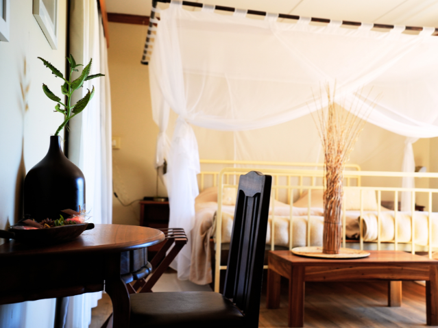 Schlafzimmer mit Himmelbett und weißem Moskitonetz in einer namibischen Lodge.